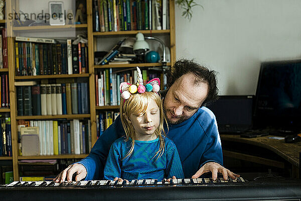 Mann bringt seiner Tochter zu Hause sitzend Synthesizer bei