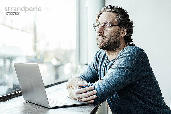 Nachdenklicher Mann mit Laptop auf dem Tisch in einem Cafe