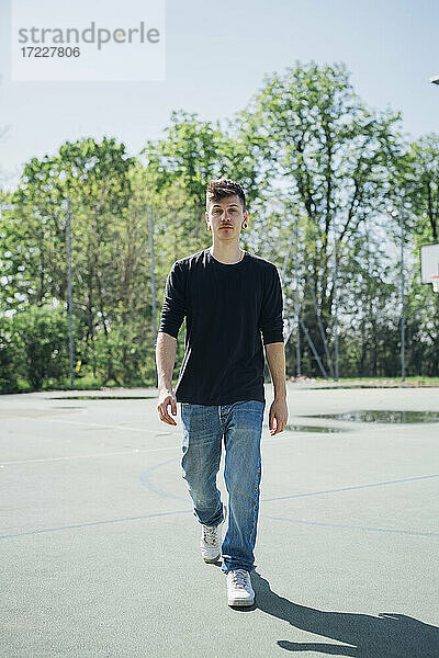 Junger Mann  der an einem sonnigen Tag auf einem Sportplatz spazieren geht