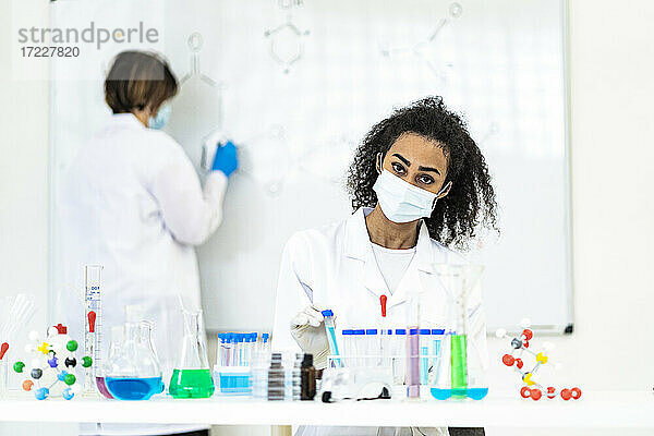 Forscherin bei der Arbeit  während ein Kollege im Labor auf einer Tafel zeichnet