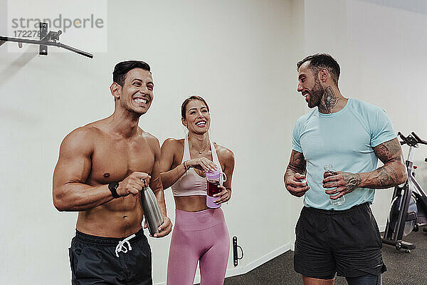 Fröhliche Sportler  die im Stehen im Fitnessstudio Wasser trinken