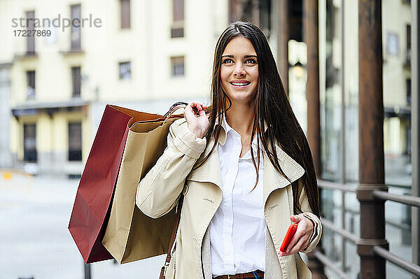 Nachdenkliche Frau mit Einkaufstüten und Smartphone in der Stadt