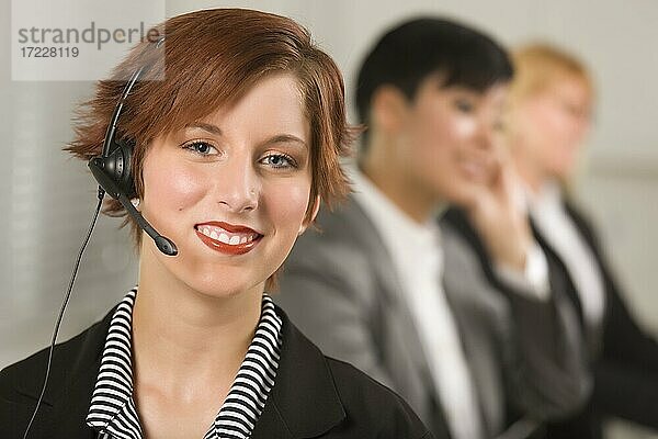 Hübsche rothaarige Geschäftsfrau mit Headset und Kollegen hinter in Büroeinstellung