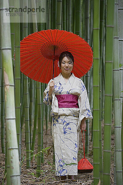 Porträt schöne junge Frau im japanischen Kimono mit Sonnenschirm unter Bambus