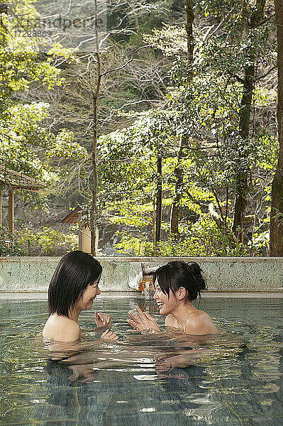 Glückliche junge Freundinnen beim Eintauchen ins Wasser im Onsen-Spa