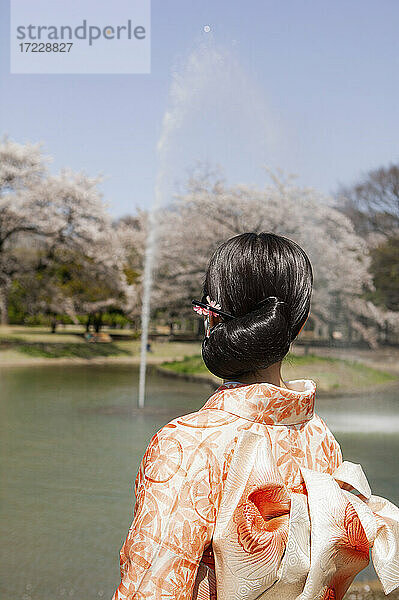 Junge Frau in orange Kimono beobachten Brunnen in sonnigen Frühling Park