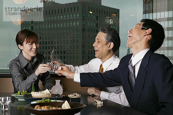 Glückliche Geschäftsleute stoßen in einem Hochhausrestaurant mit Sake an