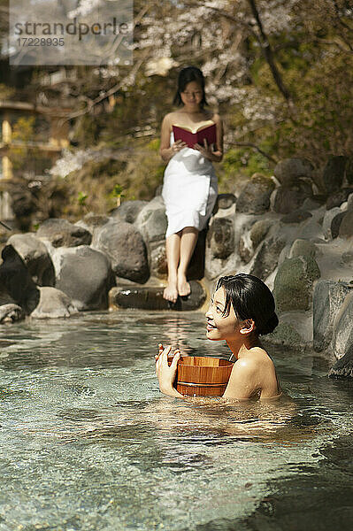 Glückliche junge Frauen entspannen am sonnigen Pool in Onsen