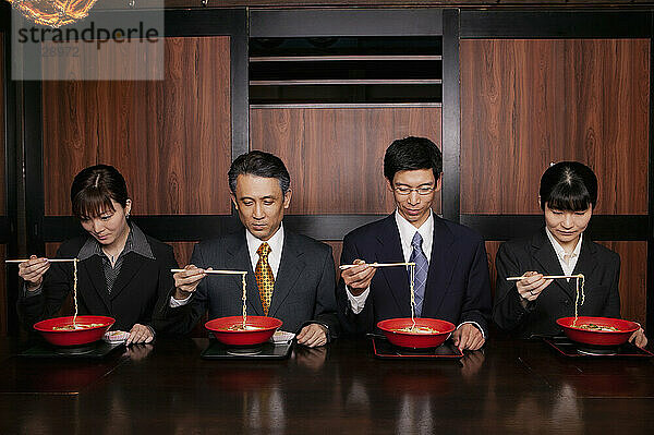 Japanische Geschäftsleute in Anzügen essen Ramen mit Essstäbchen im Restaurant