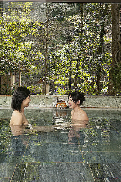 Glückliche junge Frauen  die sich unterhalten und im Onsen-Pool eintauchen