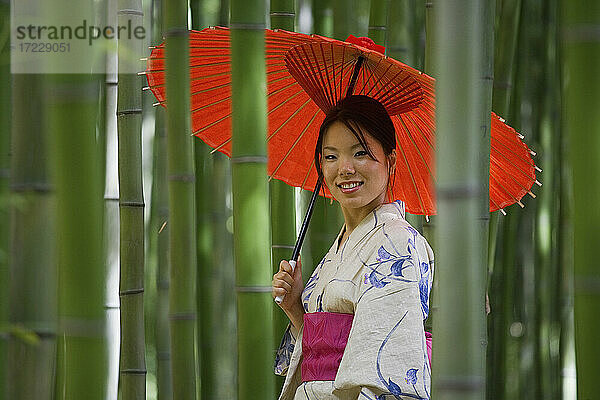 Porträt schöne junge Frau im Kimono mit Sonnenschirm unter Bambus