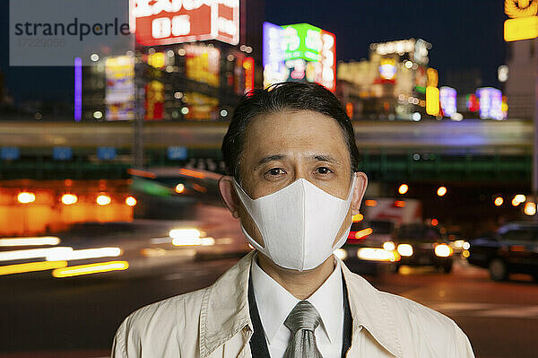 Porträt selbstbewusster Geschäftsmann mit Gesichtsmaske in der Stadt bei Nacht  Tokio  Japan