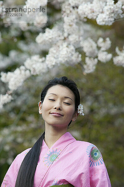Schöne heitere junge Frau im Kimono unter Kirschblüten