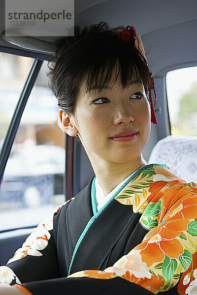 Schöne japanische Frau im Kimono auf dem Rücksitz eines Taxis
