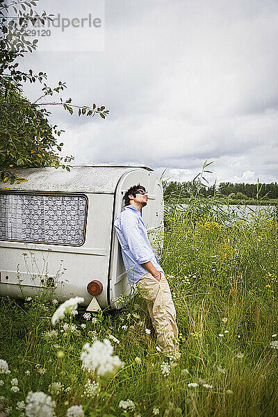 Junger Mann am Wohnwagen in idyllischer Seewiese