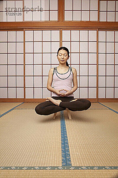 Serene junge Frau meditiert in Lotus-Pose auf Hocker
