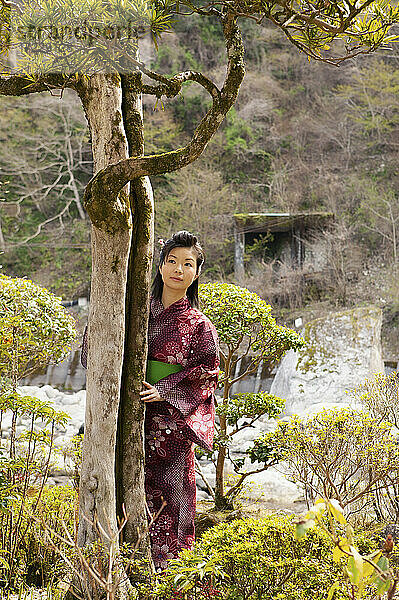 Schöne junge Frau im japanischen Kimono an Baum in ruhigen Park