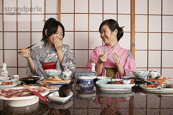 Glückliche junge Frauen in Kimonos essen Abendessen im Restaurant