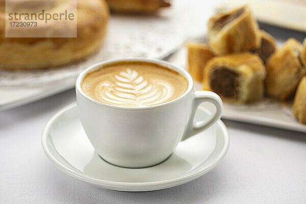 Kaffee mit kunstvollem Milchschaum-Muster und süßem Gebäck