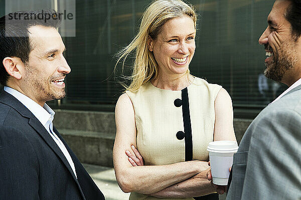 Geschäftsfrau und zwei Geschäftsleute stehen im Freien  plaudern und lächeln.