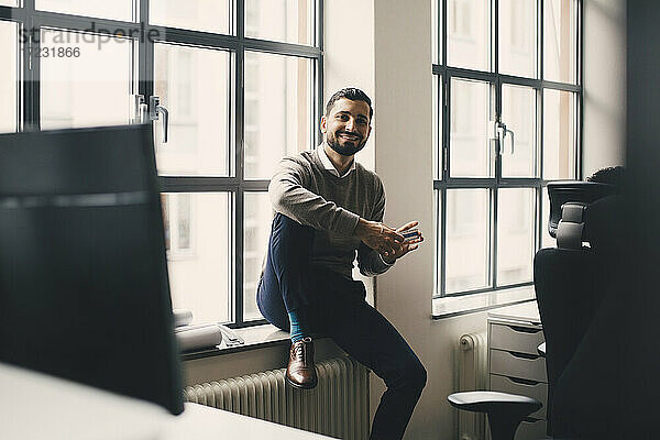 Porträt von lächelnden Geschäftsmann mit Box sitzen gegen Fenster in kreativen Büro