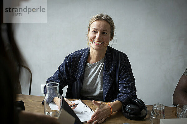 Lächelnde Geschäftsfrau  die mit einem Kollegen am Schreibtisch in einem kreativen Büro diskutiert