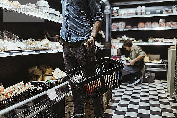 Mittelteil eines männlichen Kunden  der einen Einkaufskorb in einem Feinkostladen hält