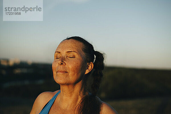 Sportlerin mit geschlossenen Augen gegen den Himmel bei Sonnenuntergang