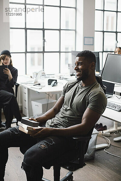 Lächelnde männliche Unternehmer mit Produkt sitzen auf Stuhl im Büro