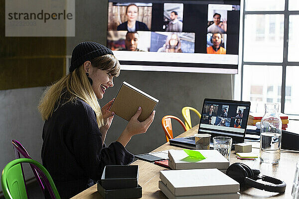 Lächelnde Geschäftsfrau zeigt Produkt an Kunden über Videokonferenz im Sitzungssaal im Büro