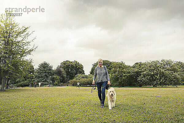 Reife Frau zu Fuß mit Hund im Park gegen den Himmel