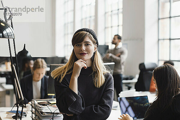Porträt einer lächelnden Geschäftsfrau mit Hand am Kinn im Büro