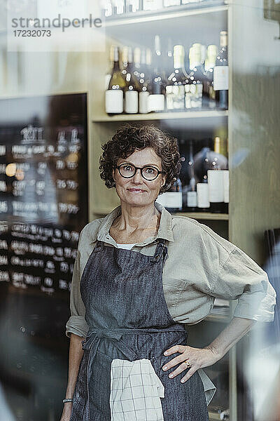 Porträt einer lächelnden Ladenbesitzerin mit Hand auf der Hüfte in einem Feinkostladen