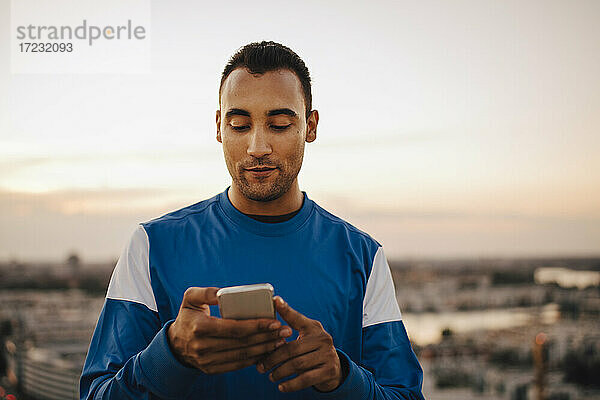 Sportler mit Smartphone gegen den Himmel während des Sonnenuntergangs