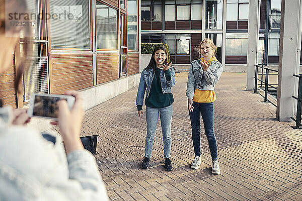 Teenager-Mädchen  das lächelnde Freundinnen auf dem Fußweg vor einem Gebäude fotografiert