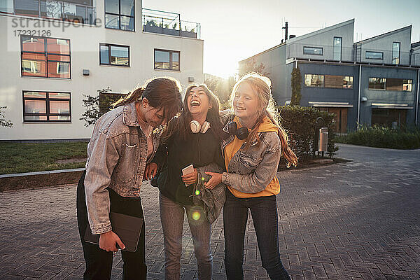Fröhliche Freundinnen lachend auf Fußweg gegen Gebäude
