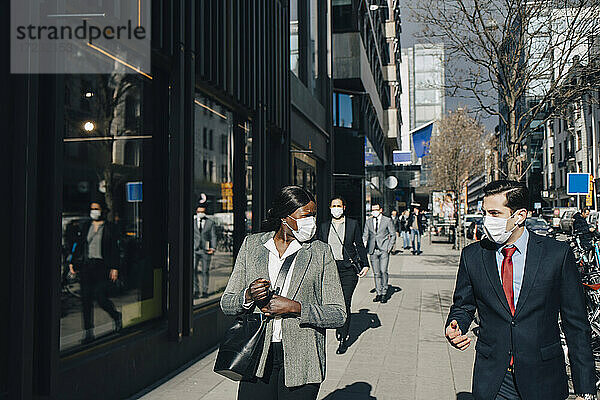 Männliche und weibliche Kollegen diskutieren beim Spaziergang an einem sonnigen Tag in der Stadt während COVID-19