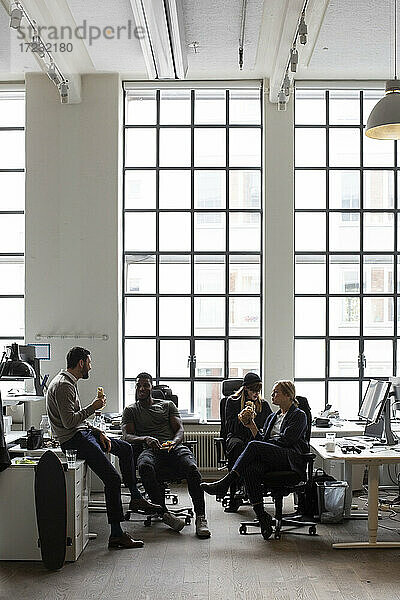 Männliche und weibliche Kollegen essen Essen  während sie im Büro sitzen