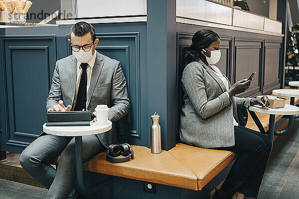 Geschäftsmann mit digitalem Tablet und Kollegin mit Smartphone in einem Café während COVID-19
