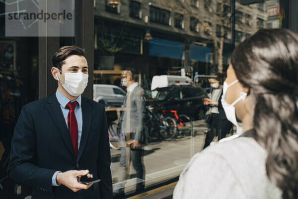 Geschäftsmann mit Gesichtsmaske im Gespräch mit einer Kollegin während einer Pandemie