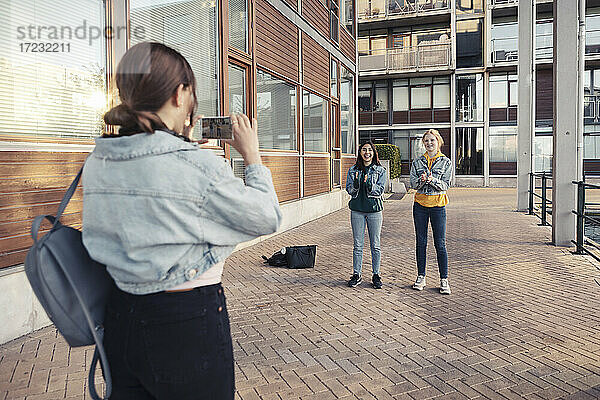 Teenager-Mädchen  das seine Freundinnen fotografiert  während es auf dem Fußweg vor einem Gebäude steht