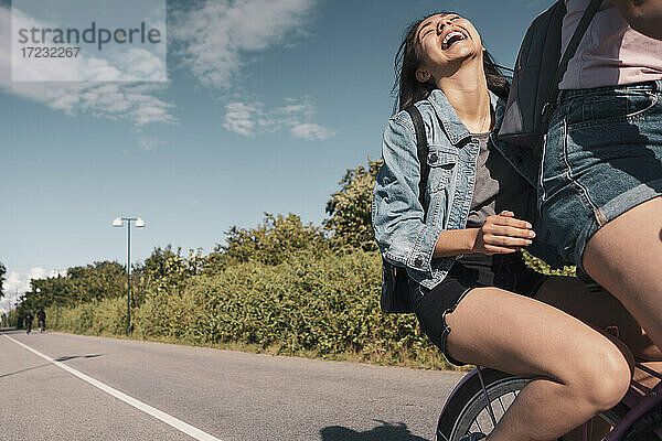 Teenager-Mädchen lachend auf dem Fahrrad sitzend hinter einer Freundin auf der Straße