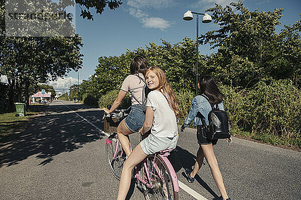 Teenager-Mädchen zu Fuß durch weibliche Freunde Radfahren auf der Straße während sonnigen Tag