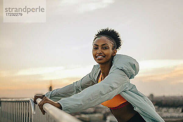 Porträt einer Sportlerin  die sich auf ein Geländer gegen den Himmel lehnt