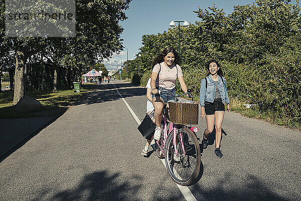 Weibliche Freunde Radfahren während Teenager-Mädchen zu Fuß auf der Straße während sonnigen Tag