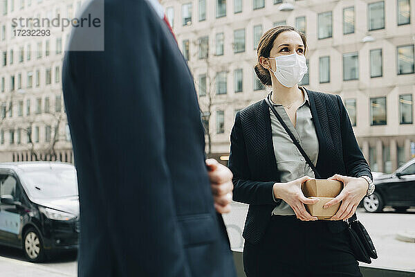 Weibliche Unternehmerin mit Kisten an der Seite eines männlichen Kollegen in der Stadt während der Pandemie