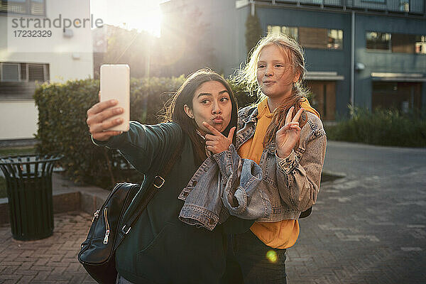 Weibliche Freunde gestikulieren  während sie ein Selfie über Smartphone auf dem Fußweg machen