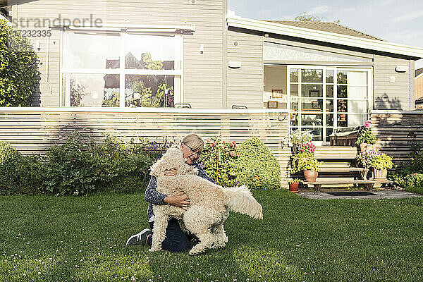 Reife Frau umarmt Hund im Vorgarten