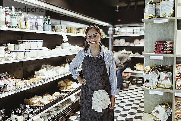 Porträt einer lächelnden Besitzerin mit Hand auf der Hüfte in einem Feinkostladen