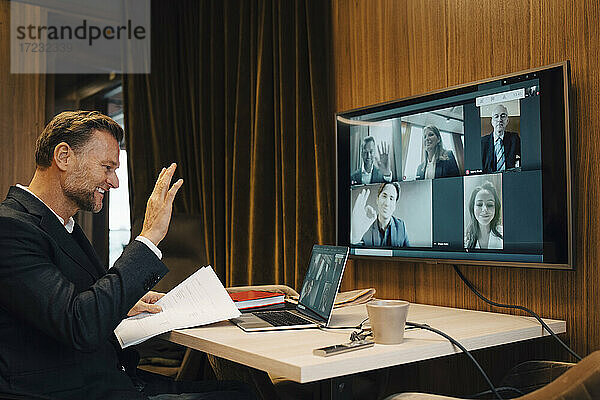 Lächelnde Geschäftsmann winken mit Kollegen auf Video-Anruf während der Sitzung im Sitzungssaal
